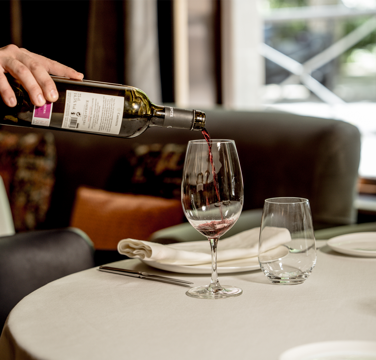 Mano sirviendo vino tinto en una copa sobre mesa preparada en el restaurante Seda Club